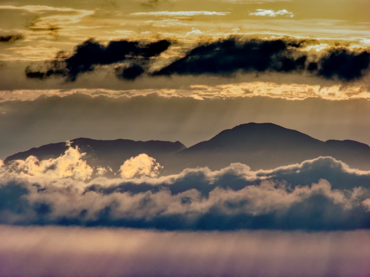 Golden light across clouds above the sea and mountain silhouette